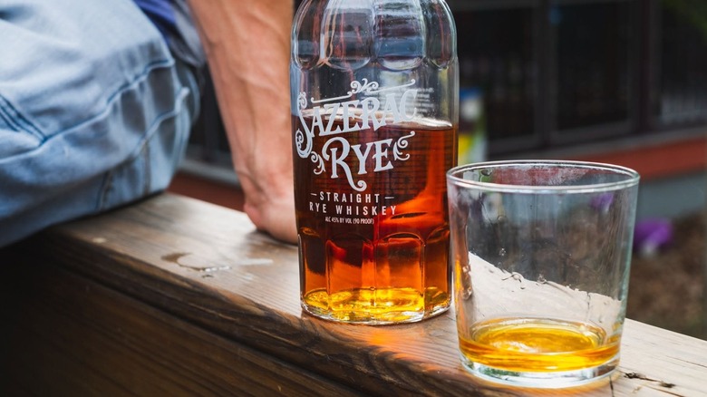 Half-empty bottle of Sazerac Rye with glass on wooden ledge outside
