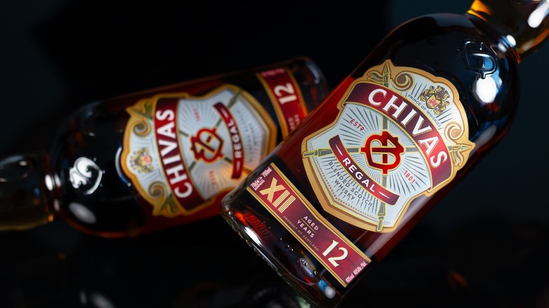 Two bottles of Chivas Regal 12 laid in different directions on a featureless dark background