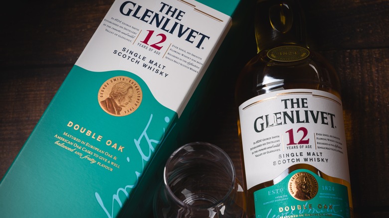 A bot and bottle of Glenlivet 12-year laying in a table with an empty whisky glass in the middle