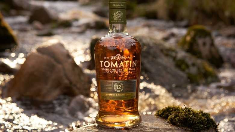 A botte of Tomatin 12-year posed on a rock with a blurred flowing water scene in the background