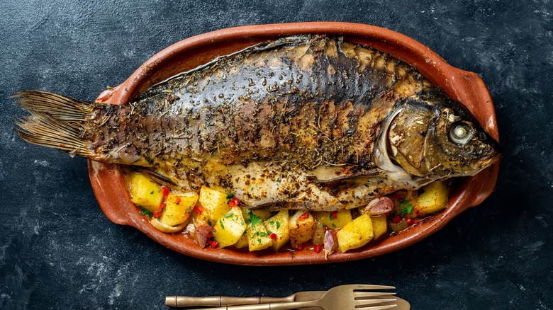 Baked carp on red platter with roasted potato wedges.