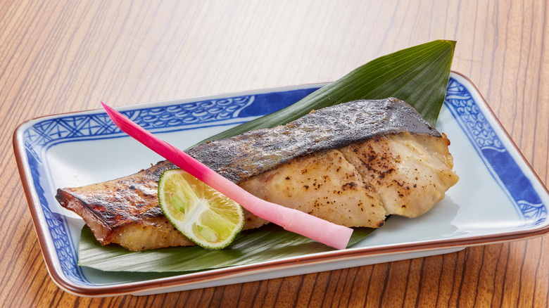 Broiled salmon filet on decorative plate with slice of lime.