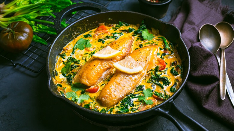 Fish filets poached in a curry sauce with herbs and vegetables in a cast iron pan.