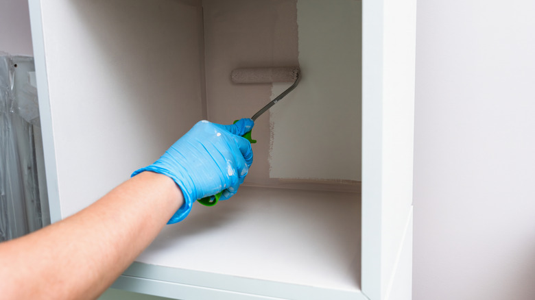 Hand applying paint with a roller inside a cabinet