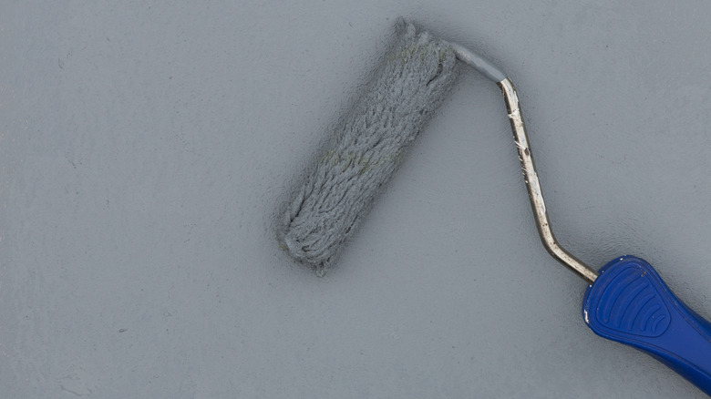 Paint roller with blue handle applying paint on gray wall