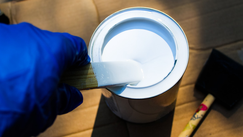 A hand wearing rubber gloves and stirring a primer can