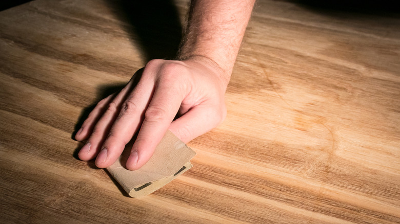 Hand running a sand paper over a wooden surface