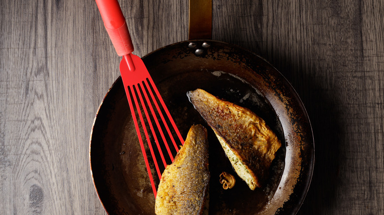 Red fish turner in a pan with 2 pieces of fish, on a wooden background