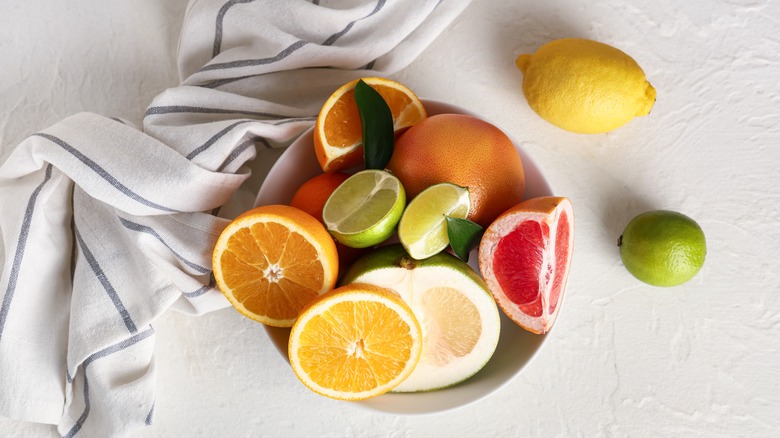 A bowl of citrus fruits on a white table with a white and blue striped napkin beside it