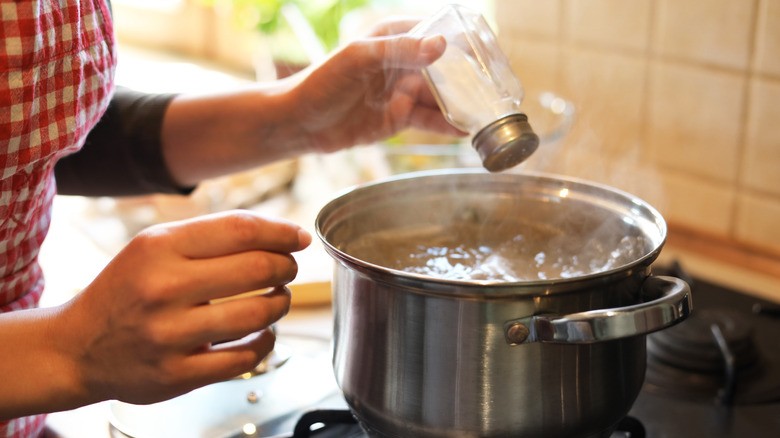 Woman adding salt to a stainless steel pot of boiling water