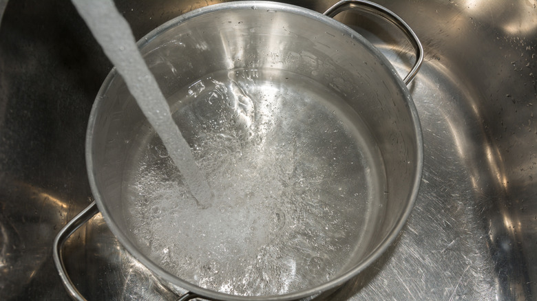 Stainless steel pan in sink with water pouring into it from faucet