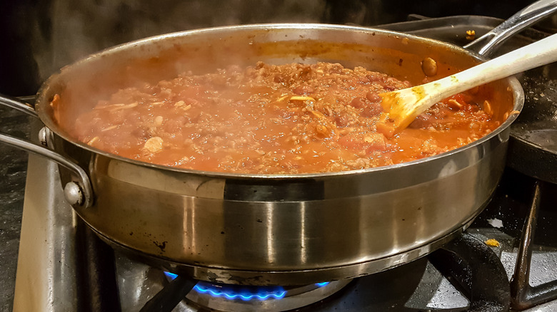 A meat- and tomato-based sauce simmering in a stainless steel pan on a gas stovetop