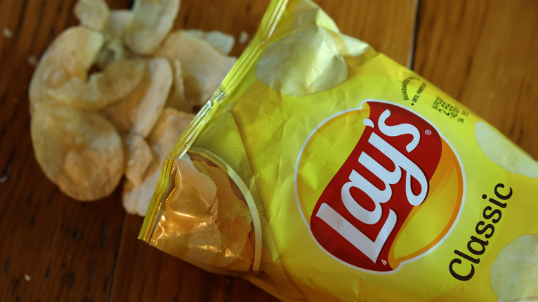 Open bag of Lay's with chips spilling on wooden table
