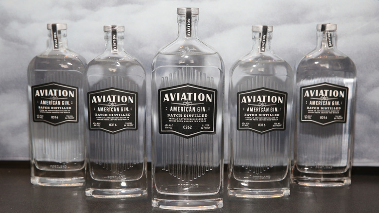 Five bottles of Aviation Gin on black table against white background.