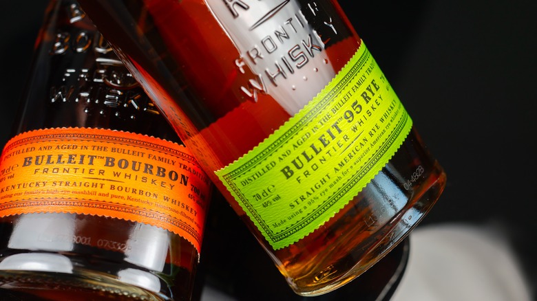 Close up on two bottles of Bulleit, one bourbon, one rye against black background.