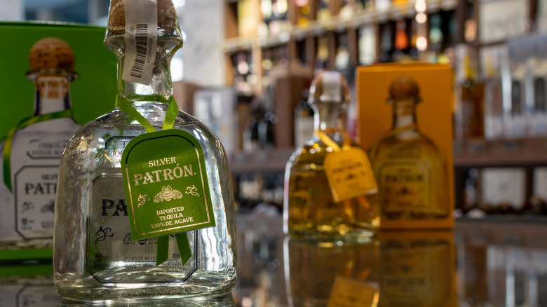 Patron Silver Tequila in focus in the foreground, sitting on a bartop. A blurry Patron Reposado sits in the background next to box.