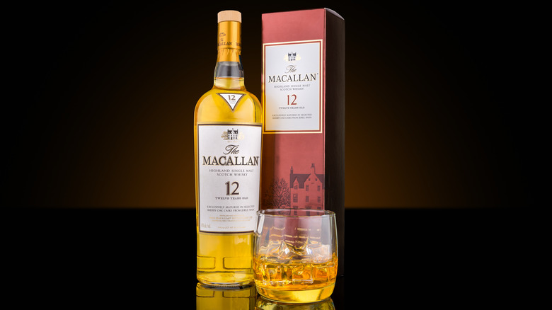 The Macallan 12 bottle next to box and glass against black background.