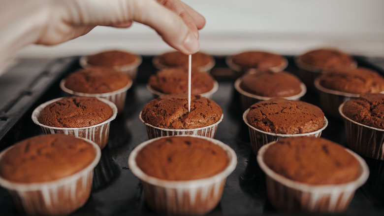 Someone places a toothpick into a cupcake on a tray
