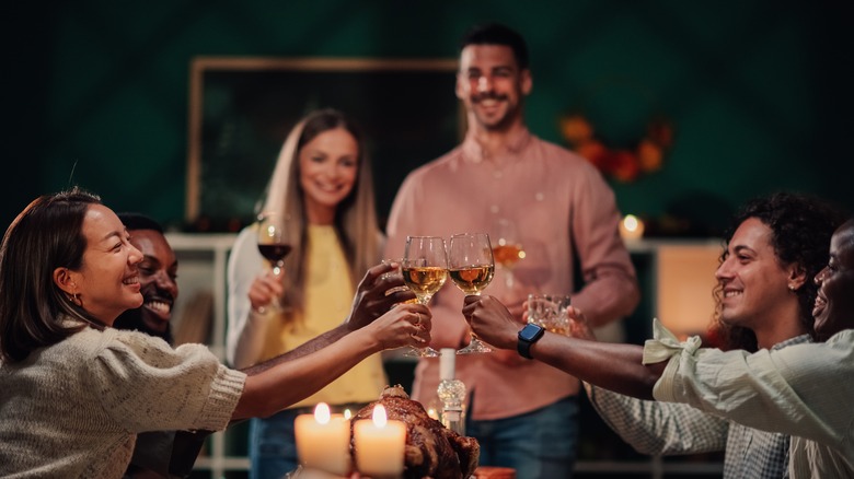 A happy group of friends toast with wine glasses over their Thanksgiving dinner table