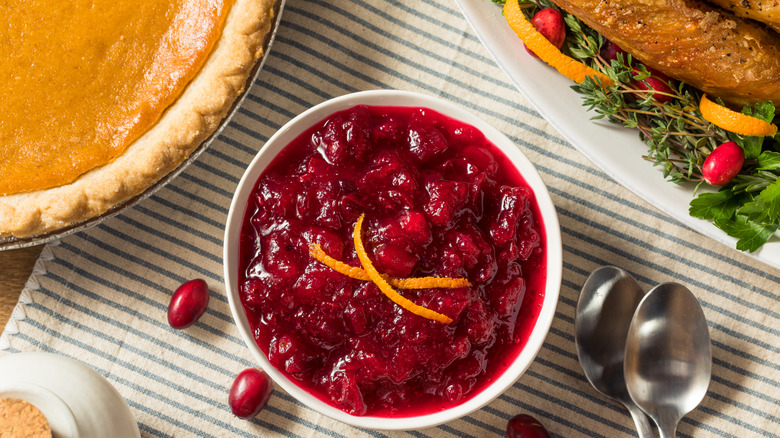 A homemade bowl of cranberry sauce on a table next to a pumpkin pie and Thanksgiving turkey