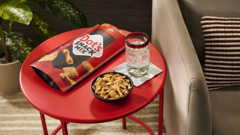 Dot's Original Snack Mix in a bowl on a red table with a beige couch, striped pillow, and houseplant nearby.