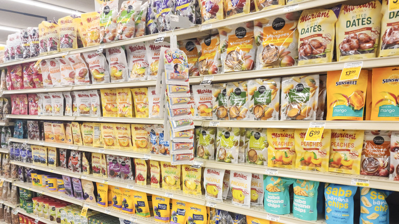Supermarket snack aisle with bags of dried fruit like dates, mangos, peaches, and banana chips.