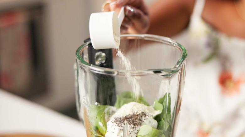 woman pouring protein powder into blender containing other ingredients