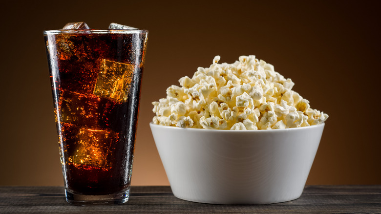 A glass of cola and a bowl of buttery popcorn