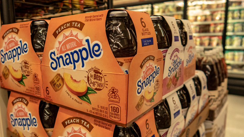 A grocery store display of six packs of Snapple peach tea
