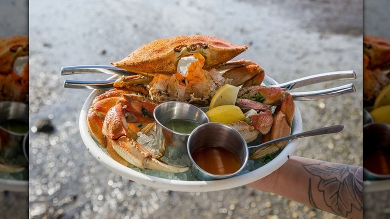 Hand holding a plate of steamed crab with a beach in the background