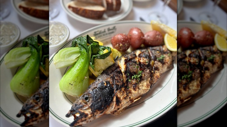 Whole grilled fish at Tadich Grill in the Bay Area on a white plate with bok choy