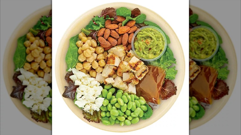 Top view of a salad bowl featuring lettuce, almonds, edamame, chicken, chickpeas, and guacamole