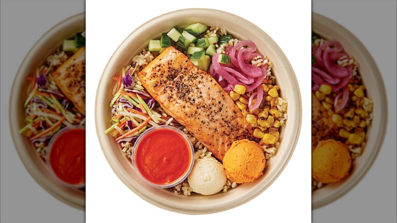 Top view of a salmon bowl with vegetables, two pastes, and sauce