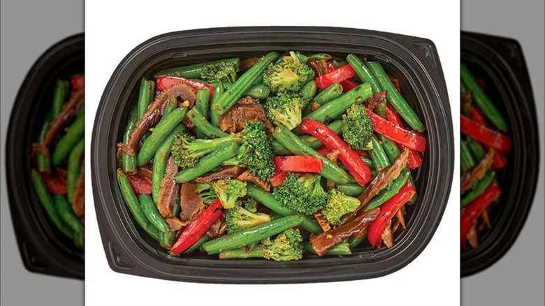 A plastic meal container with a stir fry of beef and vegetables