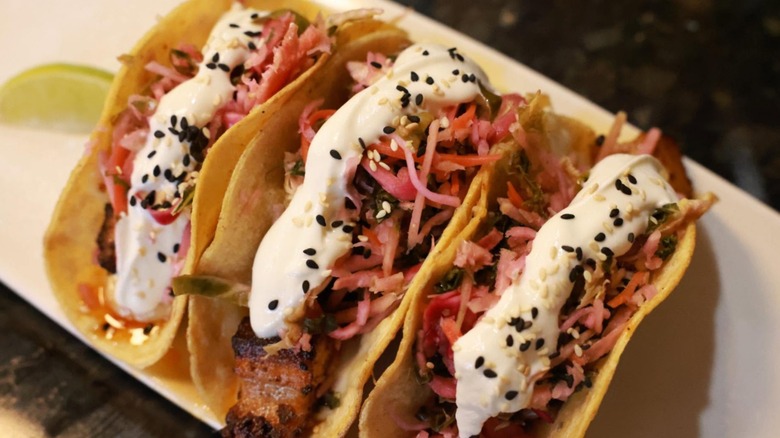 A close-up of taco with pickled red onion, black sesame seeds, and a creamy sauce
