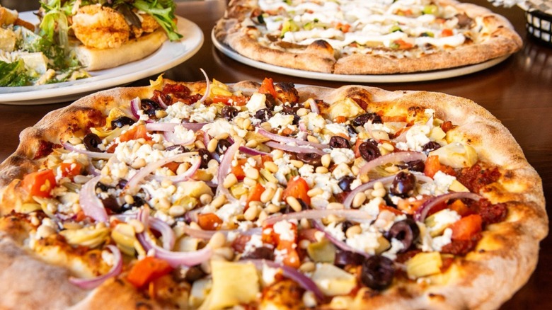 A close-up of a Neapolitan pizza with lots of toppings and another pizza and a sandwich in the background