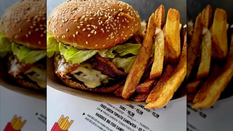A bacon cheeseburger with thick-cut fries in a paper basket on top of the menu for Jim's Drive-In