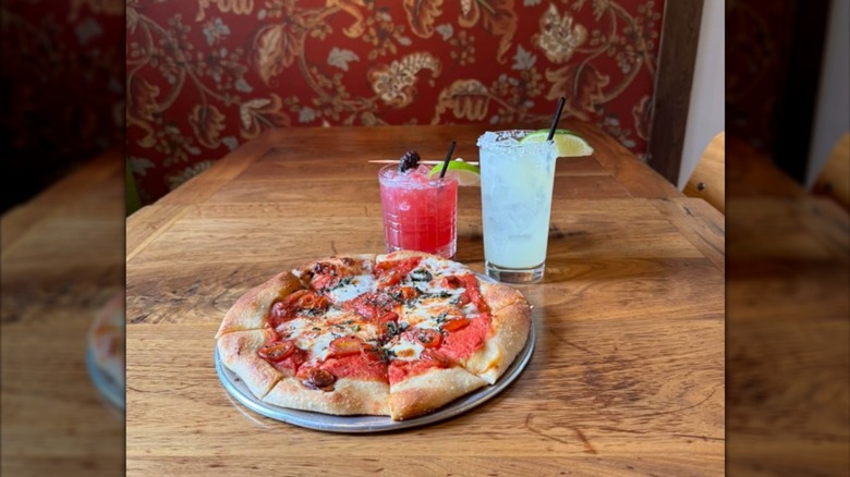 An artisinal pizza next to two coktails ona  table at The Humble Tomato