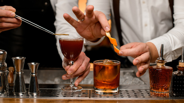 Bartenders adding garnishes to 2 cocktails