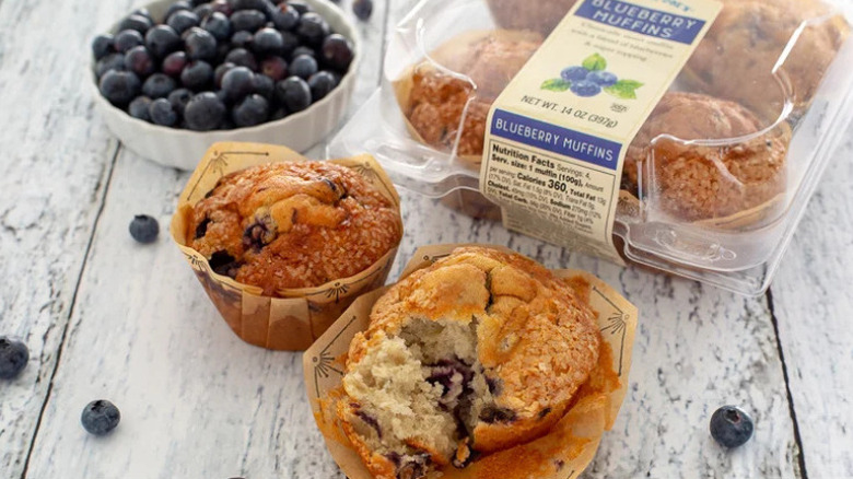 Plastic container of streusel-topped Trader Joe's Blueberry Muffins on white wooden table
