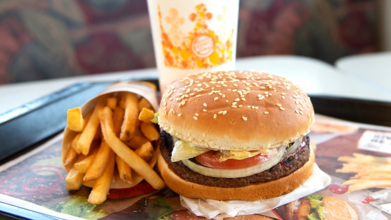Burger King Whopper burger next to sleeve of fries and drink cup on black tray