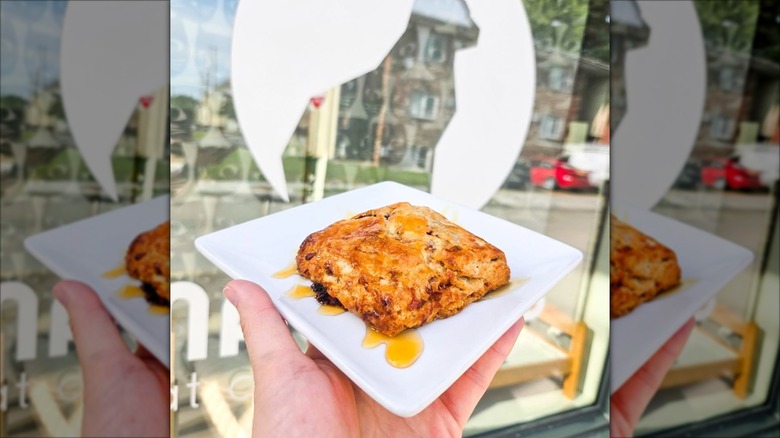 Hand holding scone on plate in front of Mauhaus logo with cat silhouette
