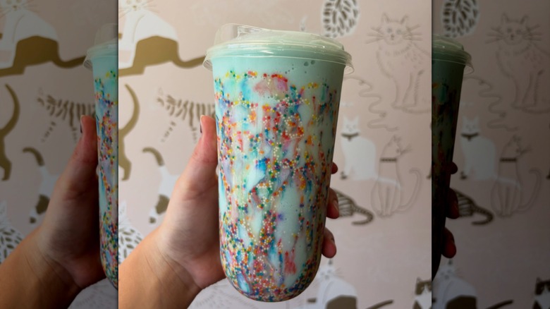 Hand holding cotton candy themed drink in front of wall with cat illustrations