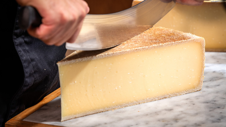 a large wedge of Gruyère being sliced