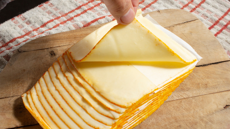 a hand lifting up a slice of Muenster cheese