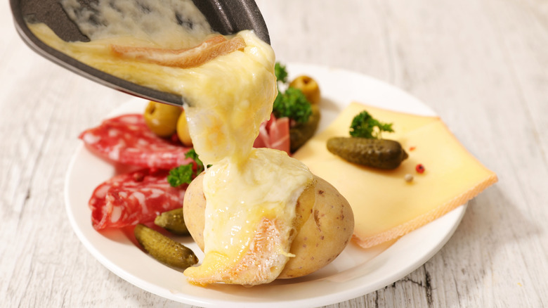 melted Raclette being poured onto a plate with potato, salami, and cornichons