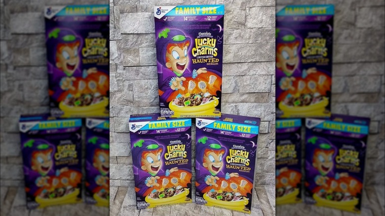 Three boxes of Chocolate Lucky Charms with Haunted Marshmallows sit in a pyramid formation in front of a stone wall.