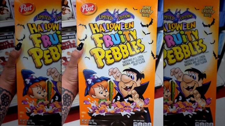 A person holds a box of Halloween Fruity Pebbles in a grocery store aisle.
