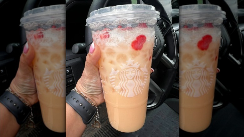person holding Starbucks Mango Dream Coconut Milk Refresher in their car