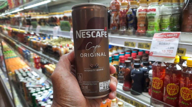 A person holding canned Nescafé coffee in a store.
